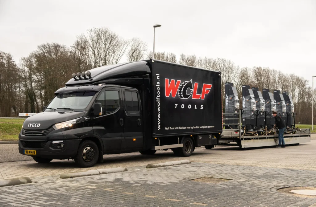 Leeuwis Equipment Wolf Tools WTTL8500W Set Van 4x 8,5 Ton Draadloos 34 Ton Totaal - Transport Van Een Reeks Nieuwe Verpakte Hefkolommen Op Een Aanhanger Achter Een Zwarte Wolf Tools Bestelbus